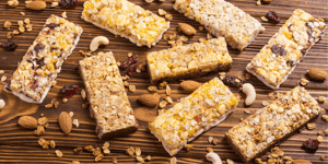 Barrette proteiche croccanti con cereali, frutta secca e frutta disidratata su sfondo di legno rustico. Uno snack nutriente e gustoso, ideale per chi cerca energia e benessere in ogni momento della giornata.