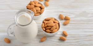 Caraffa di latte di mandorla accanto a ciotole colme di mandorle intere, simbolo di freschezza e naturalità. Una delle bevande vegetali più amate, sana alternativa al latte tradizionale.