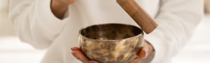 Primo piano di una persona che suona le campane tibetane con un bastoncino di legno, durante un bagno sonoro: un’esperienza sensoriale che favorisce rilassamento e benessere energetico.